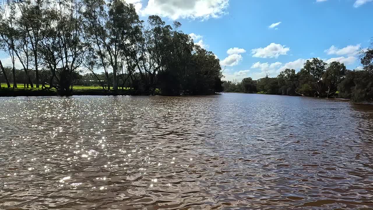 A serene river scene with sunlight glistening on the water under a clear blue sky, boat passing by