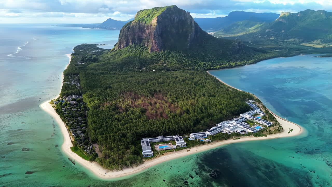 Ilmakuva dronella Mauritiuksen Le Morne Brabantin niemimaasta, näyttäen koralliriuttoja, turkooseja laguunivesiä ja ikonisen vuoren kohoavan trooppisen rannikon yläpuolelle.