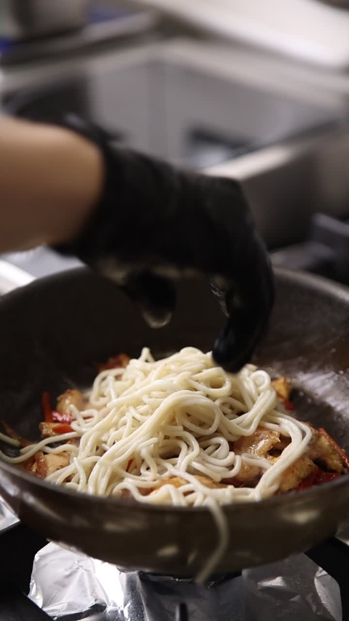 シェフがフライパンの鶏肉と野菜に調理済みの麺を加える