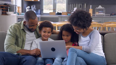 Familia-Sentada-En-Un-Sofá-En-Un-Salón-Abierto-Usando-Una-Computadora-Portátil