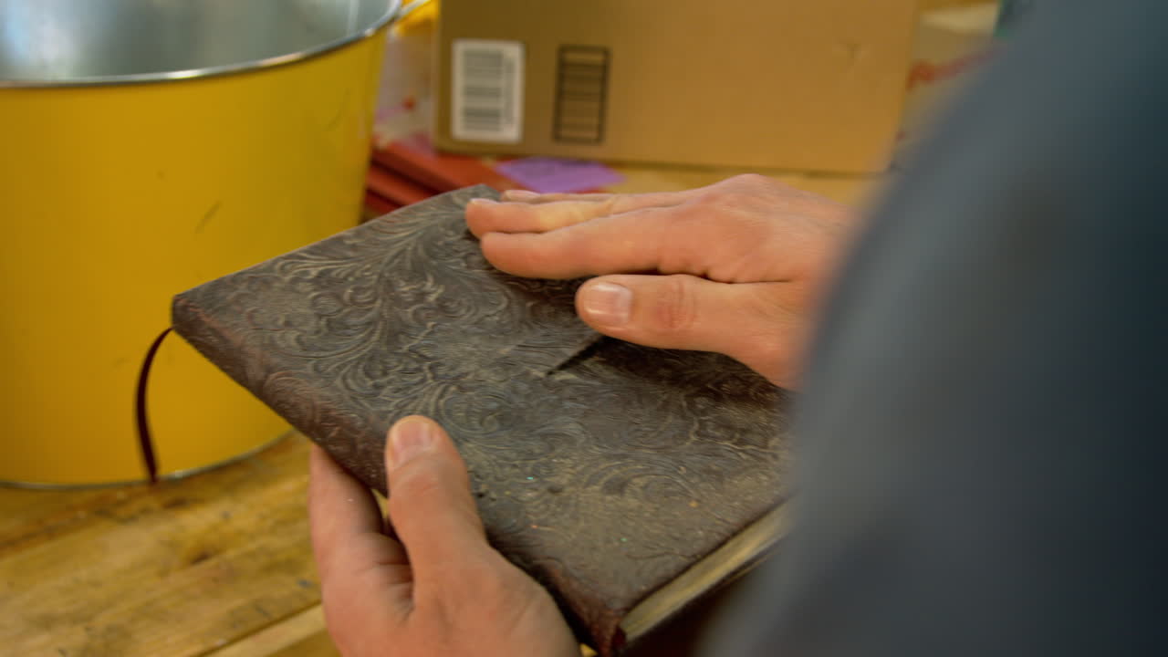A man finds an old or antique leather bound notebook or journal that is dusty and blows the dust off.