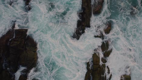 Aerial-top-down-view-moving-upwards-from-large-waves-crashing-against-the-rocks-in-the-Pacific-Ocean-of-Mexico,-Oxaca