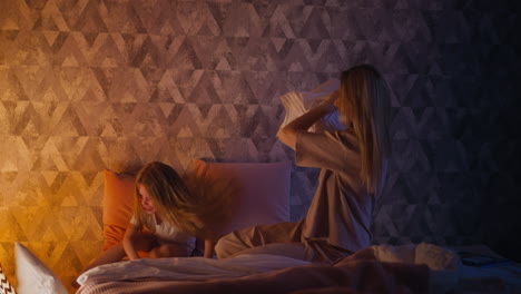 Joyful-girl-drops-down-pillow-fighting-with-mother-on-bed