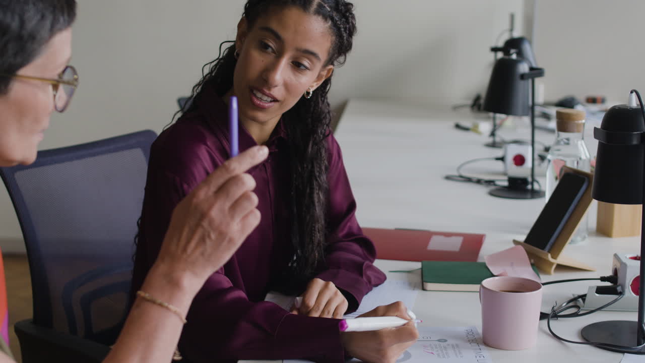 Two professional women collaborating and writing at a desk in an office