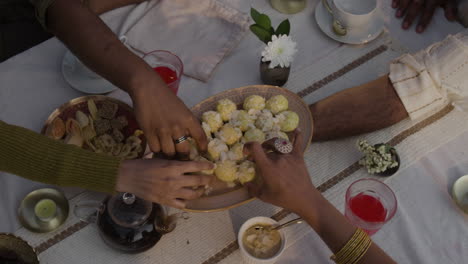hands reaching for traditional sweets and snacks at a festive table