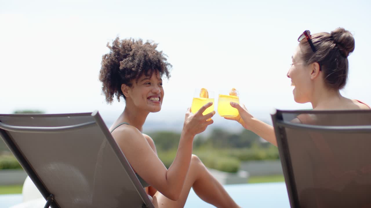 Diverse women friends swimsuit-clad poolside left woman smiling toasting with yellow drinks sipping
