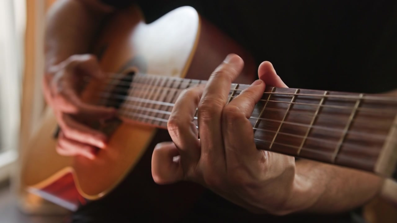 Primo piano di una persona che suona musica su una chitarra classica acustica, eseguendo un assolo al rallentatore con la tecnica fingerstyle. Il video presenta un'illuminazione bella e calda e un'alta qualità estetica visiva.