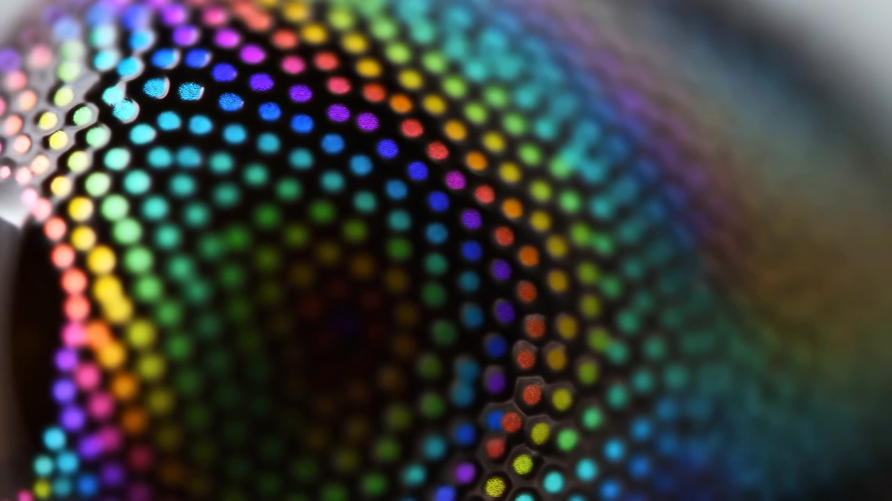 Colorful iridescent reflections move across curved perforated mesh, revealing repeating circular holes, glossy contrast, soft blur, and abstract geometric texture with vibrant rainbow tones for