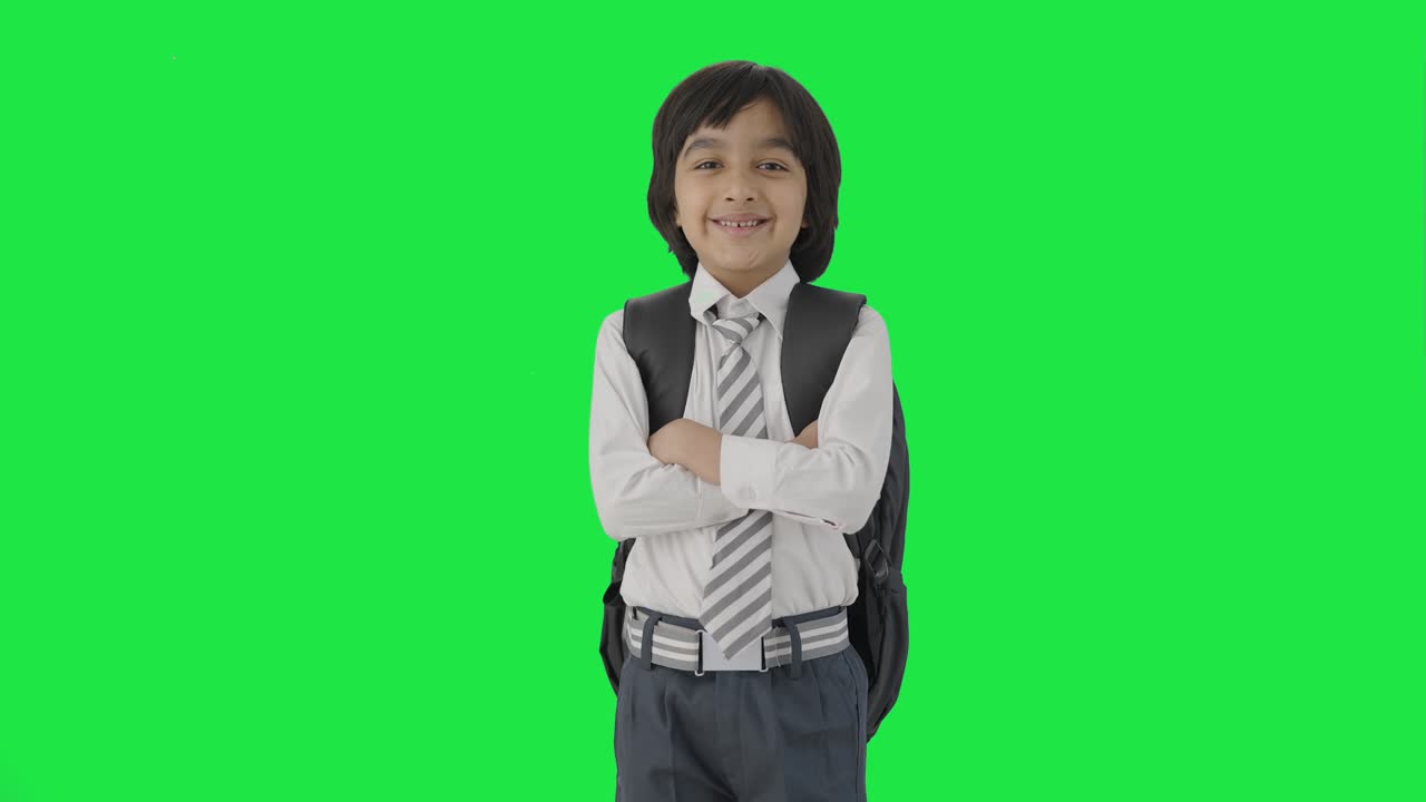 niño de escuela indio feliz de pie con las manos cruzadas pantalla verde