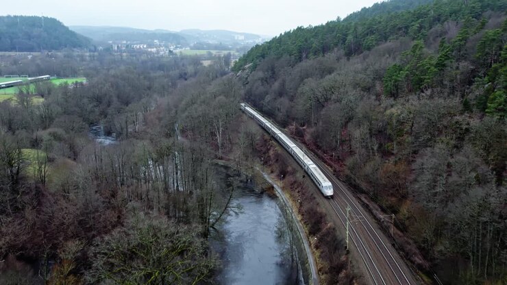 Passenger's Train Passing Through Railway By The Mountain Covered With Dense Forest In Jonsered, Sweden. - aerial shot