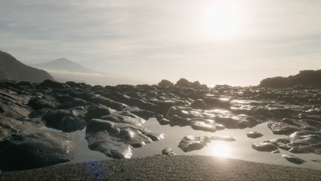 morning beach black sand rocks and sun reflection in tide pools, playa de la arena tenerife canary island, vertical pan