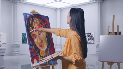 side view of asian female artist enjoys painting a girl on canvas by oil paints and brush in gallery