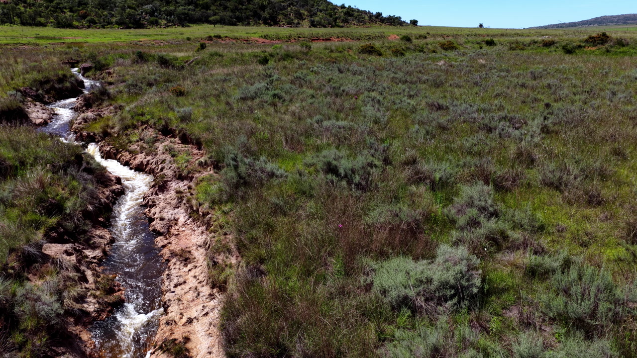 Strong stream cutting through rugged iron stained channel in open grassland