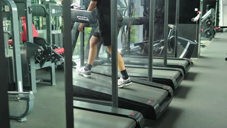 adult male in athletic wear walks steadily on a treadmill in a well-lit, contemporary gym with exercise equipment visible. stable camera, natural lighting