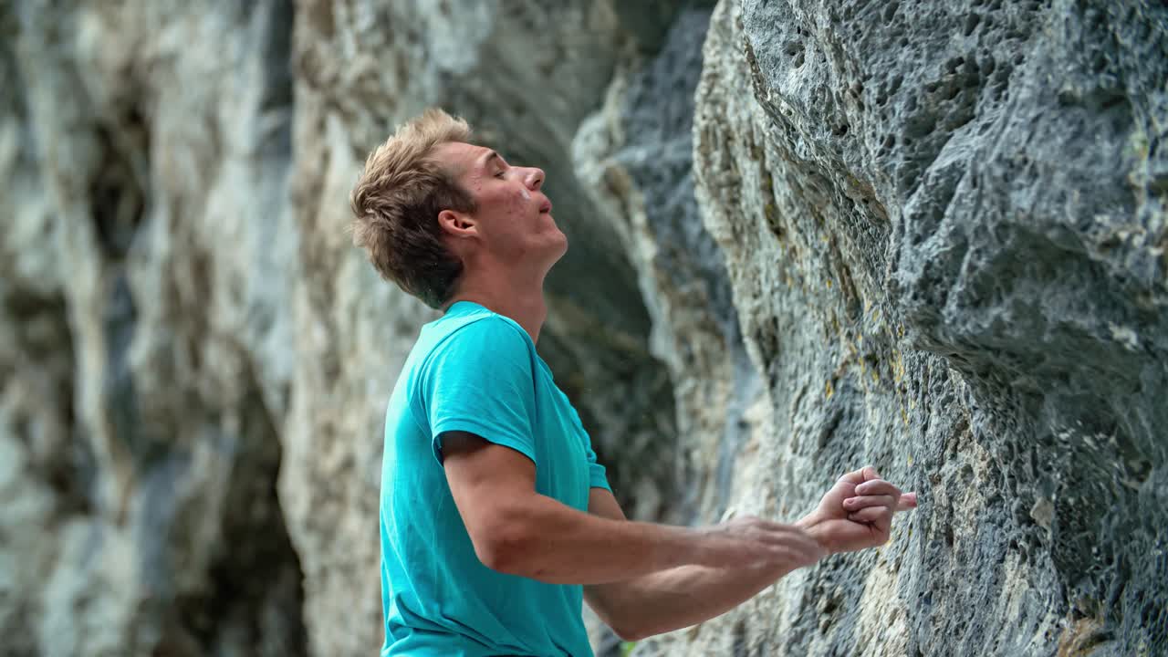 Athletic young man climbing a rough high wall with no rope or asecuration, just relying on his hand strength and endurance