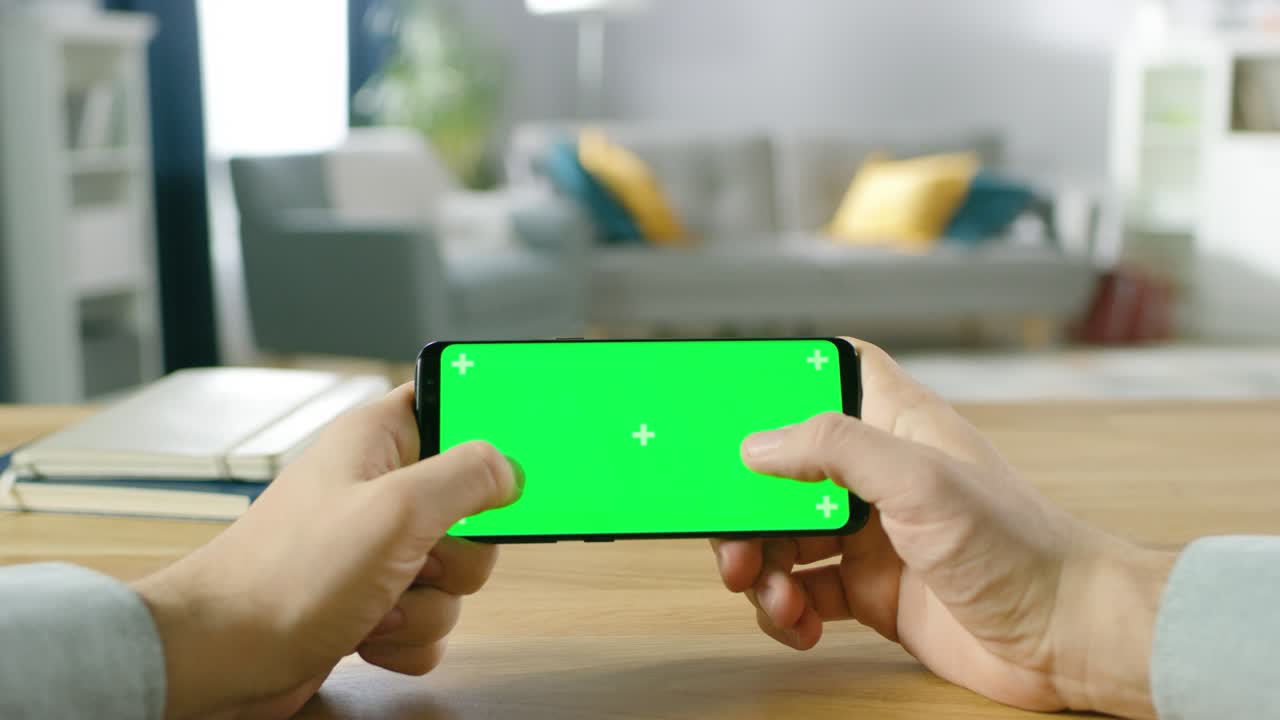 초록색 스크린 스마트폰을 고 엄지손가락으로 게임을 하는 남자의 1인칭 클로즈업입니다.