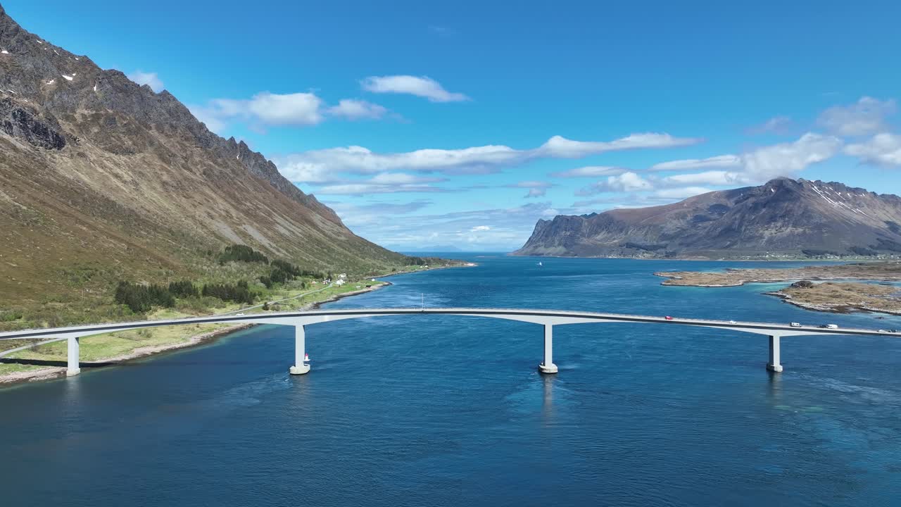Ascending aerial revealing Gimsoy Bridge, channel, mountains, and E10 traffic in Lofoten