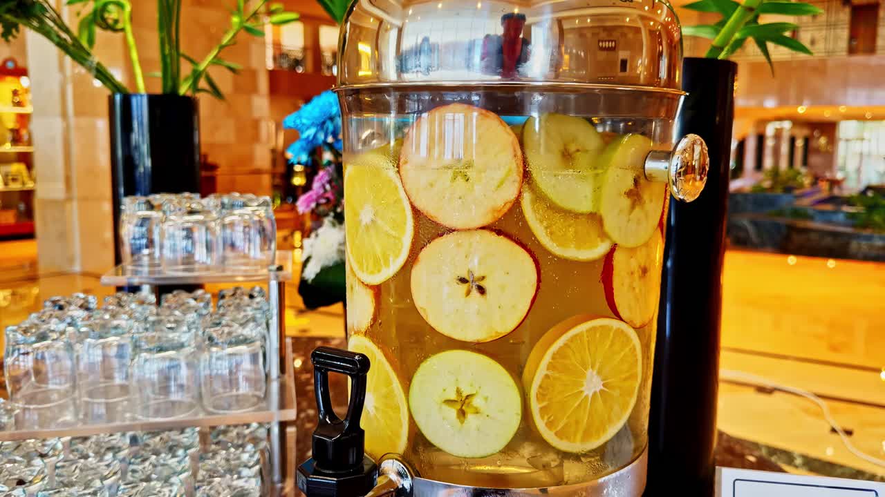Close-up of citrus fruit infused water dispenser in a bright indoor refreshment area
