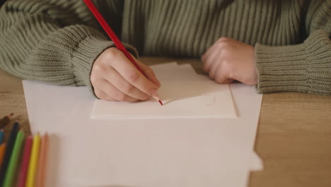 vista de cerca de las manos de una niña escribiendo una carta a santa claus sentada en una mesa