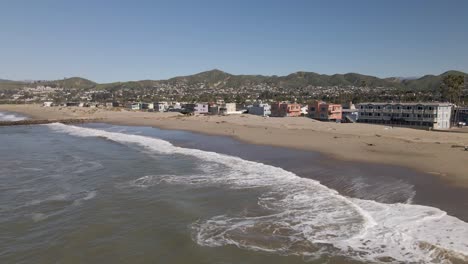 vuelo bajo de drones capturando las olas tranquilas de la playa de ventura, la orilla arenosa, las casas frente a la playa, y vislumbres de la ciudad de ventura