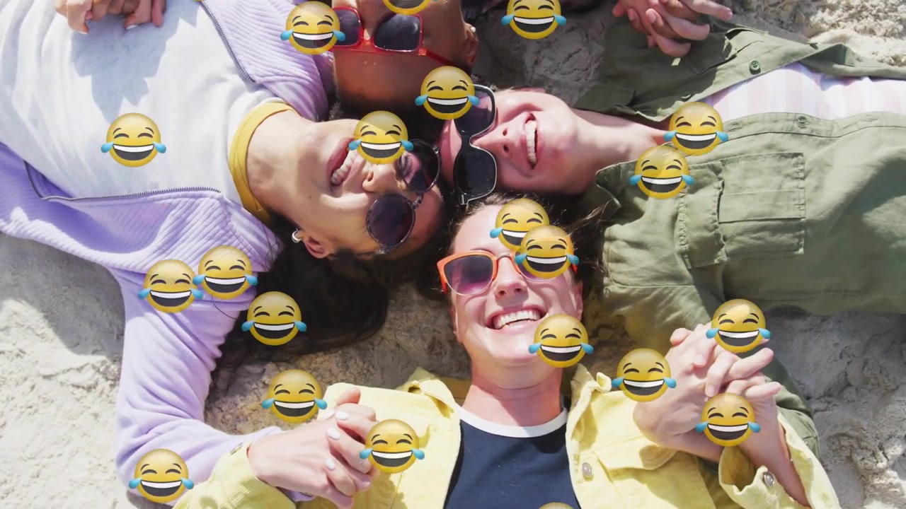 Vertikales Video: Liegende Frauen mit Sonnenbrillen, Händchen haltend, lachend im Sand, Emoji-Einblendung erscheint