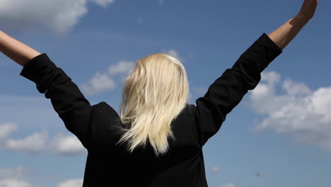 back view of blond businesswoman is standing with raised arms on blue sky background