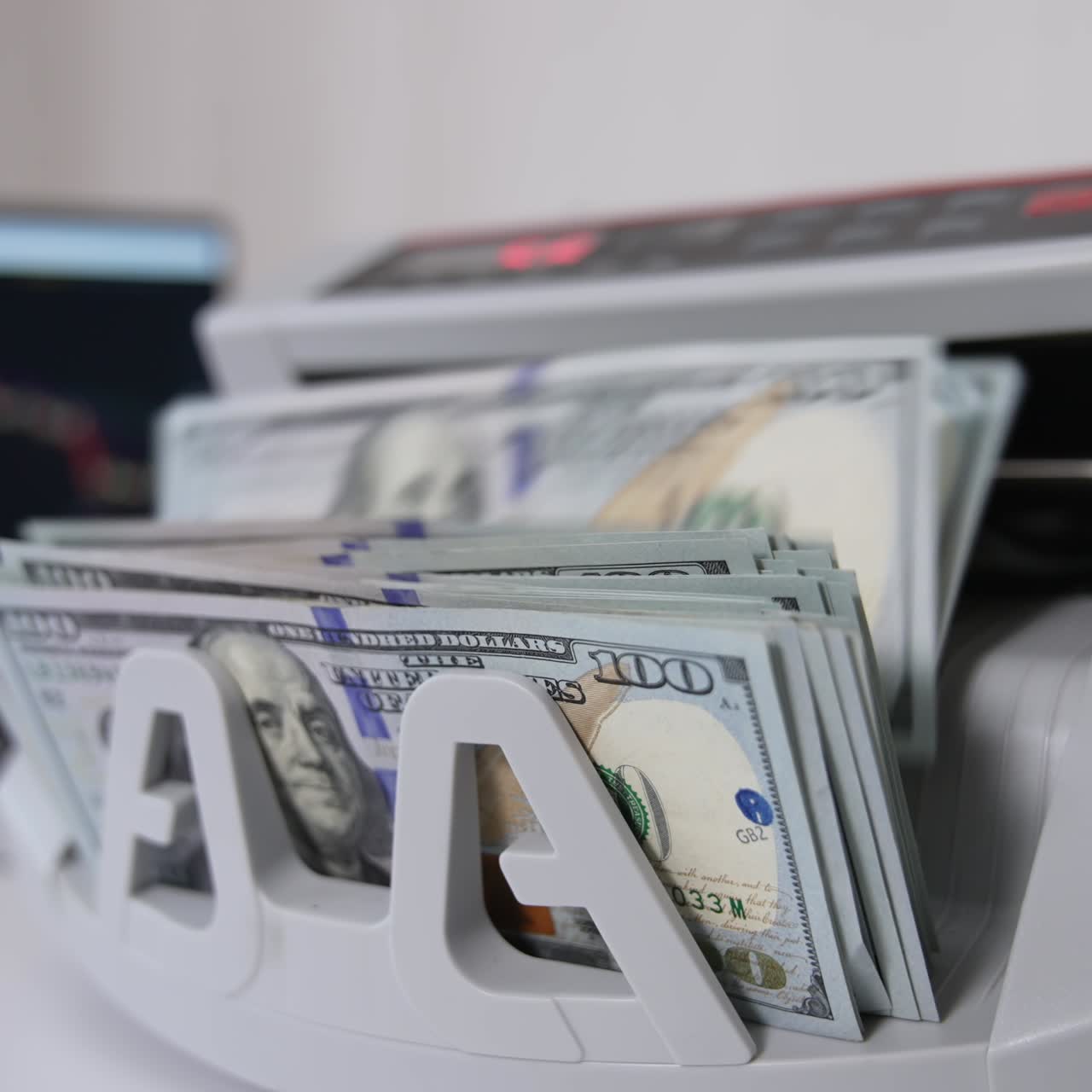 A hand switches on money counting machine. A wad of hundred dollar bills is being put into equipment for cash calculation. Close up. Blurred backdrop