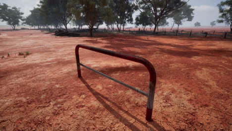 a rusty metal gate stands in the middle of a red dirt outback landscape