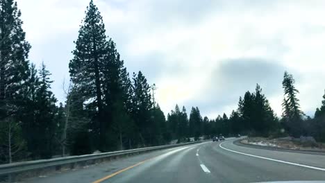 dramatic time lapse shot of a car as it travels down a country highway through snowy mountains, pine trees clouds, other vehicles can been seen in the adjoining lanes