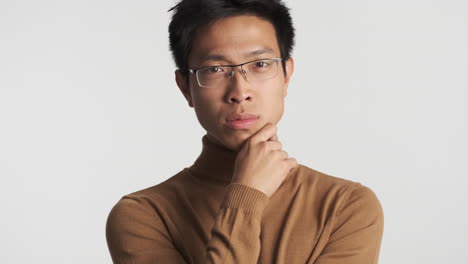 pensive asian man in eyeglasses looking at the camera.