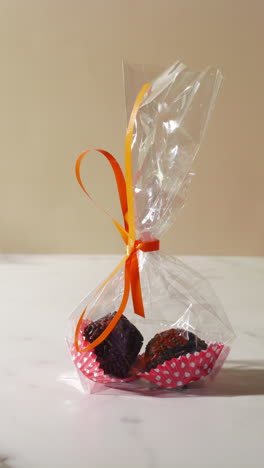 close-up of a hand taking a clear gift bag containing two chocolate truffles in red polka dot wrappers, tied with an orange ribbon. bright lighting highlights the festive and elegant presentation.