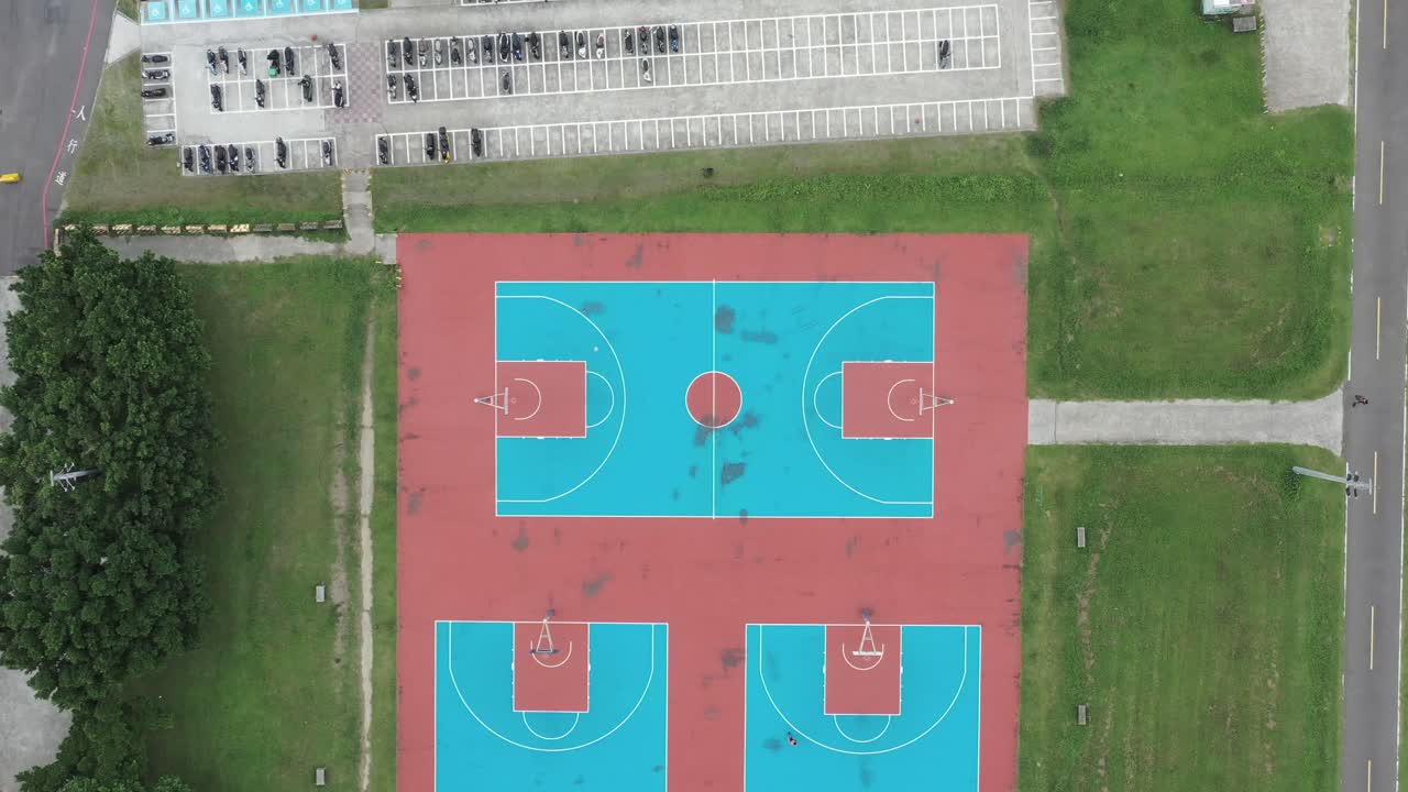 4K drone aerial top-down shot of outdoor basketball courts with players, surrounded by green park and trees