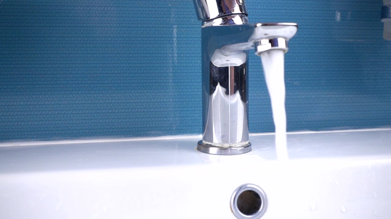 Water from the bath mixer flows into the washbasin in the bathroom. Slow motion.