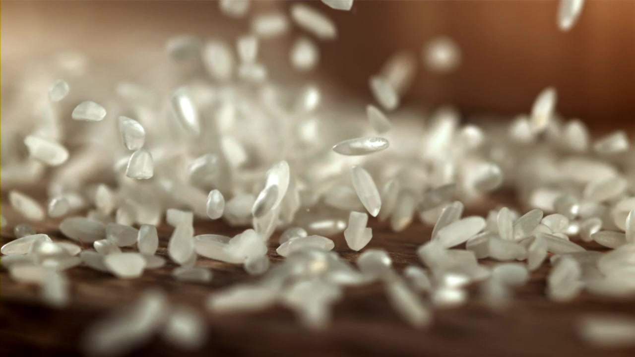 Chicchi di riso bianco crudo che cadono su una superficie di legno al rallentatore