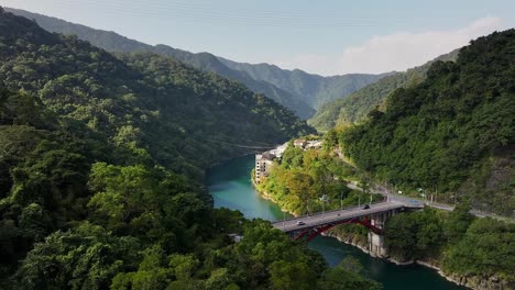 aerial panning shot of cars on bridge crossing river in green mountains of wulai, taiwan