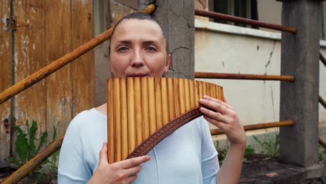 una mujer joven tocando una flauta de pan cerca de una casa antigua