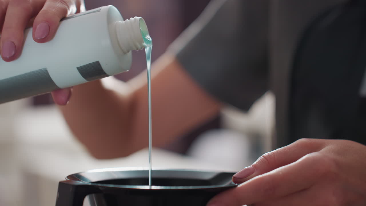 professional stylist pouring developer into bowl, closeup scene of hairstylist mixing hair dye carefully, detailed shot showing stylist meticulously pouring developer into mixing bowl for coloring