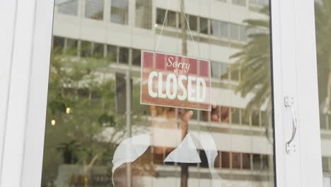 sad african american male barista wearing black apron turning sign and closing cafe