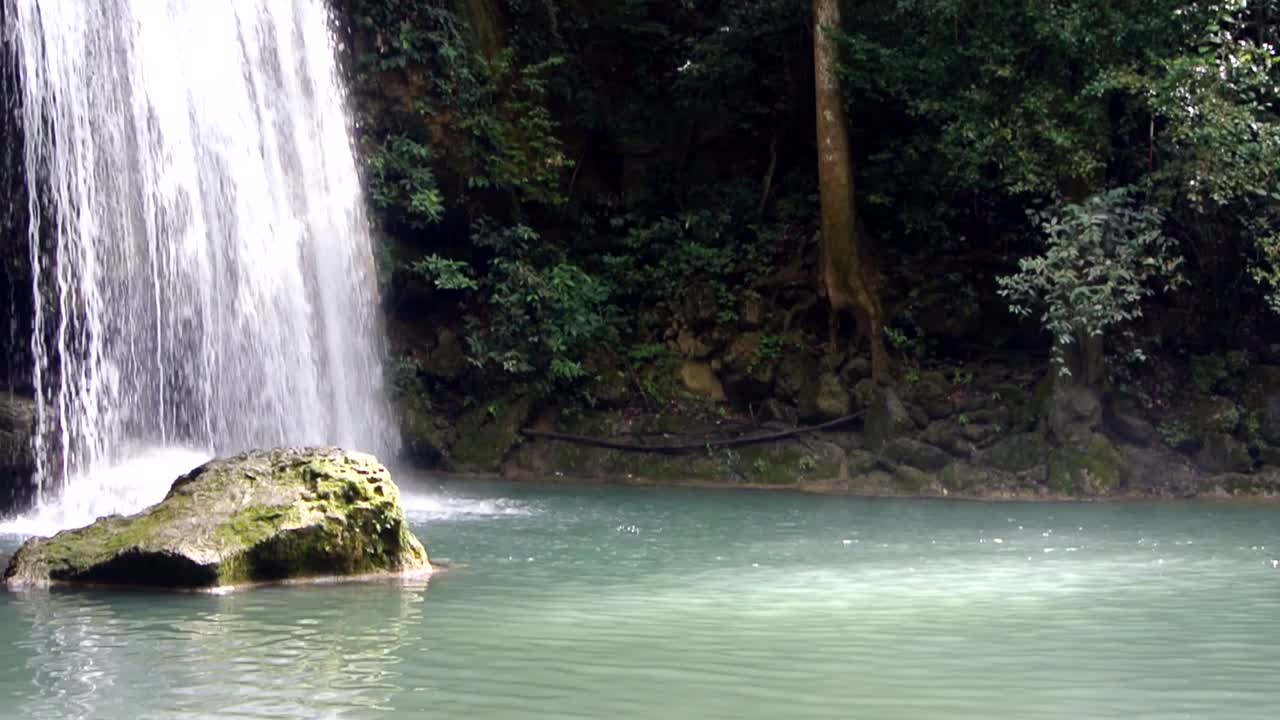 cascada tropical que se vierte en una piscina azul fresca dentro de una gran jungla escénica y roca en primer plano