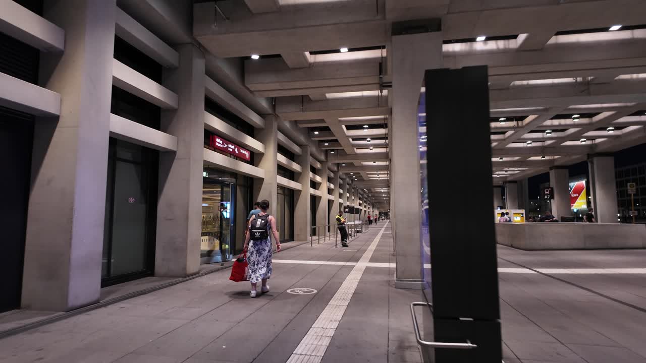 A view of a spacious airport corridor with travelers walking at Berlin Brandenburg Airport. The scene captures a modern architectural atmosphere with an urban feel.