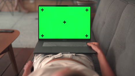 woman lying on couch using laptop with green mock-up screen. girl watching something on computer