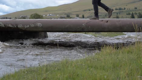 big pipe over the furious stream of a river, man walks on it first from right to left and then left to right