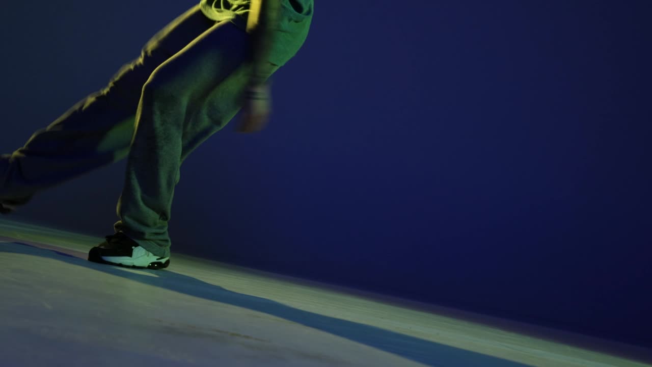 Male legs, hip-hop dancer dancing isolated over dark blue background in neon light. Modern dance art, fashion, youth, ad, style. 4K, video