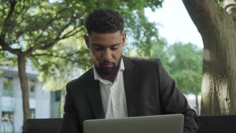 Focused-young-businessman-working-with-laptop-in-sunny-park.