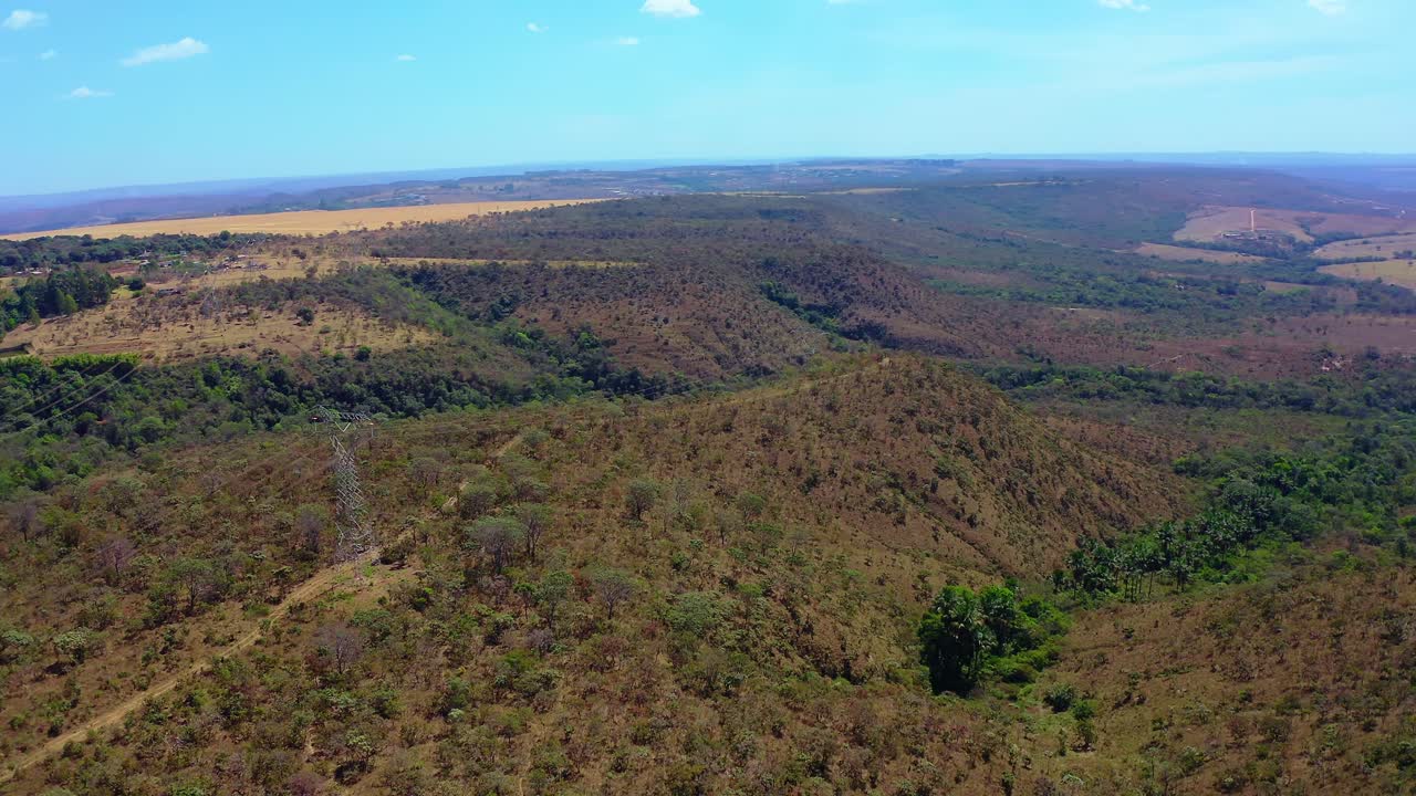 Aerial panorama capturing water spring creating lake amid Brazilian Cerrado's dry bushes, scattered green trees, nestled within expansive valley landscape under clear azure sky
