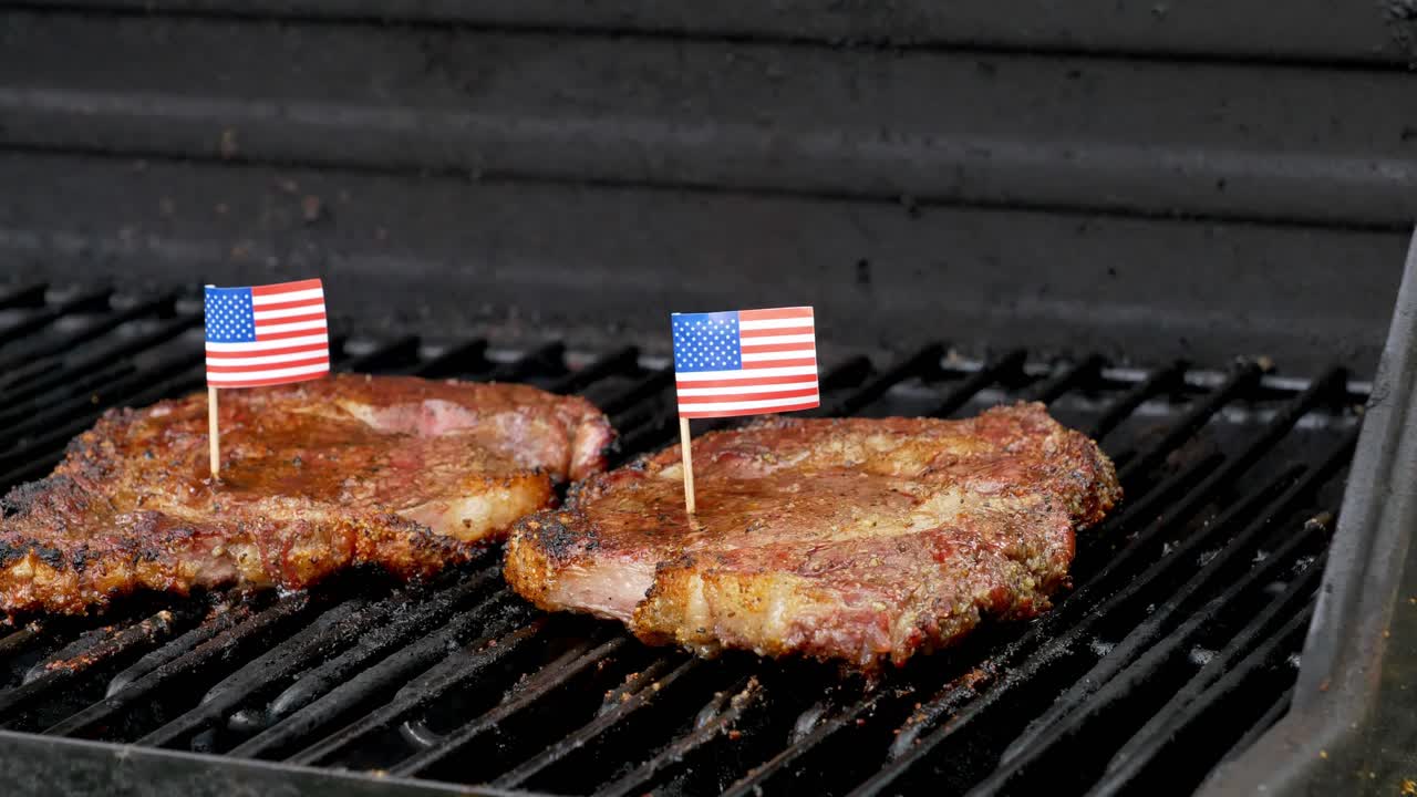 una maravillosa foto de dos jugosos filetes de costilla sentados en la parrilla y cocinándose con dos pequeñas banderas americanas encima con palillos de dientes
