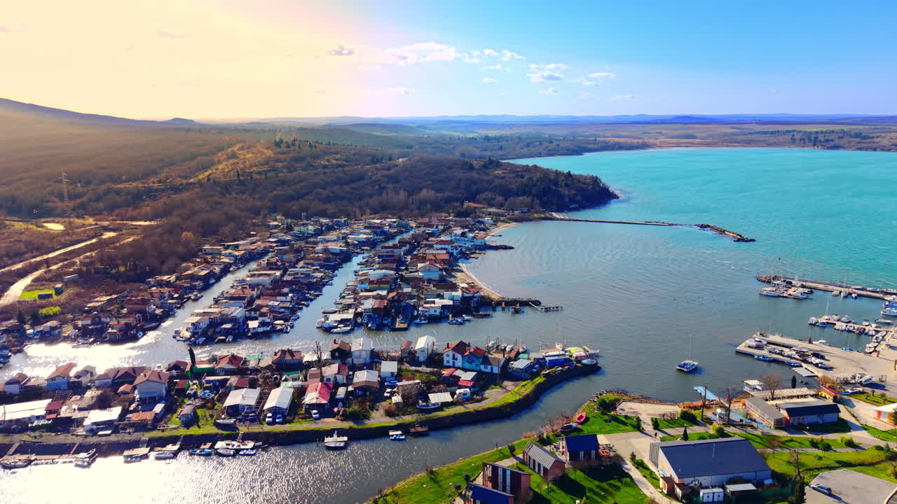 Insediamento costiero con case colorate, un canale fluviale e un piccolo porto sulla costa del Mar Nero. Vista aerea di un villaggio di pescatori e marina al tramonto.