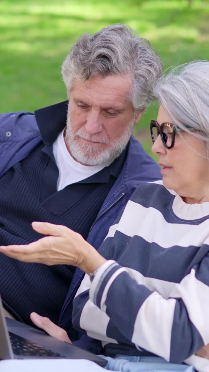 Coppia matura che discute di contenuti su un portatile in un parco
