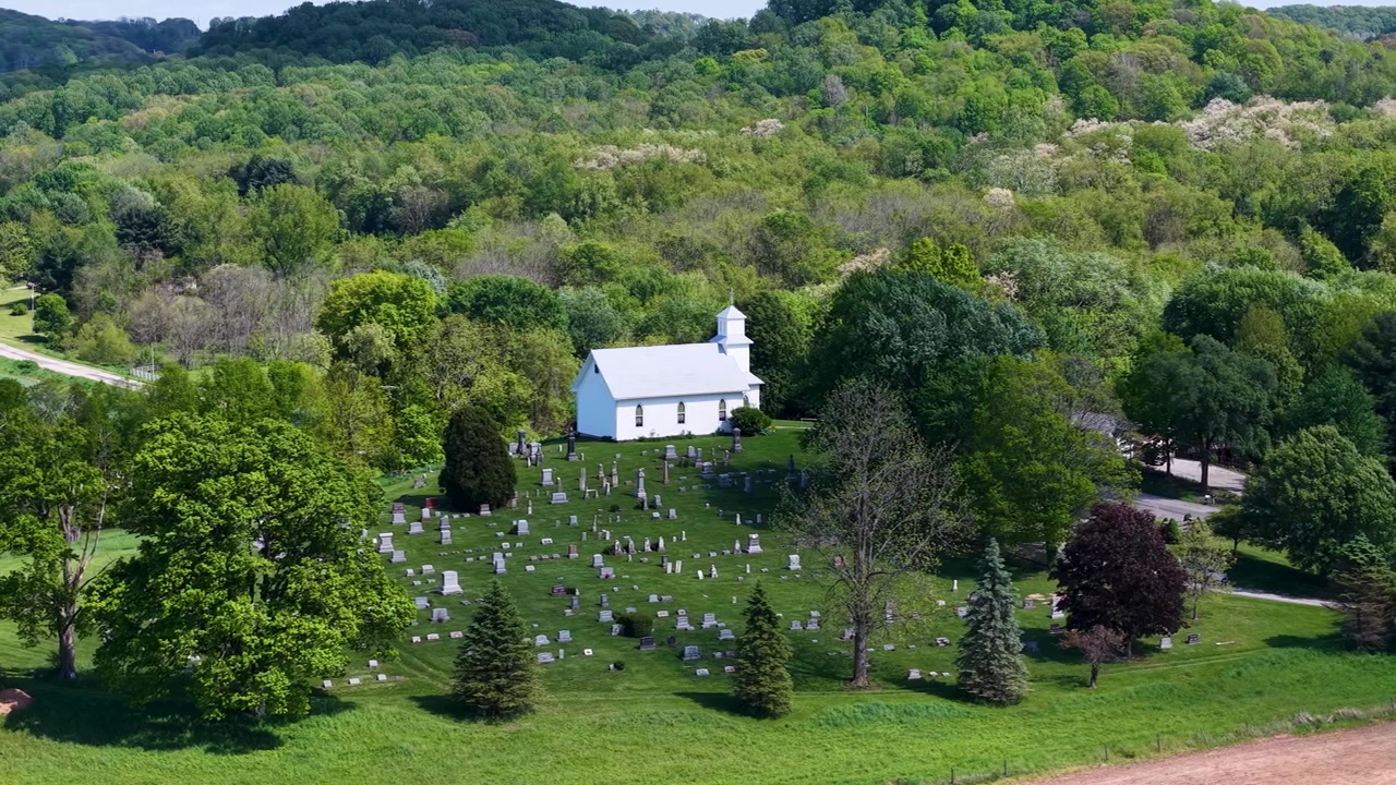 Luchtfoto van een witte kerk te midden van boomgaardbomen met een bordeauxrode sierboom nabij het terrein
