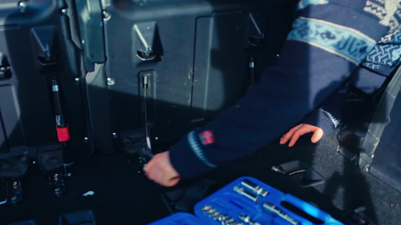 A Person is Working Inside a Pajero, Using a Ratchet Wrench to Remove Bolts Near the Rear Seat Area, With a Toolkit Placed Nearby - Close Up